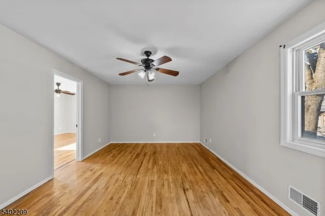a view of empty room with wooden floor and fan