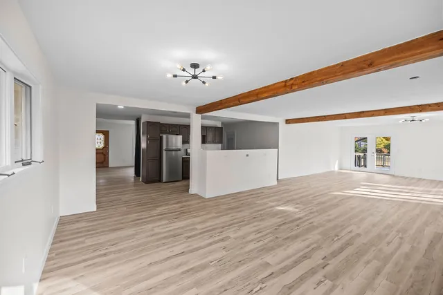 a view of an empty room with wooden floor and kitchen view