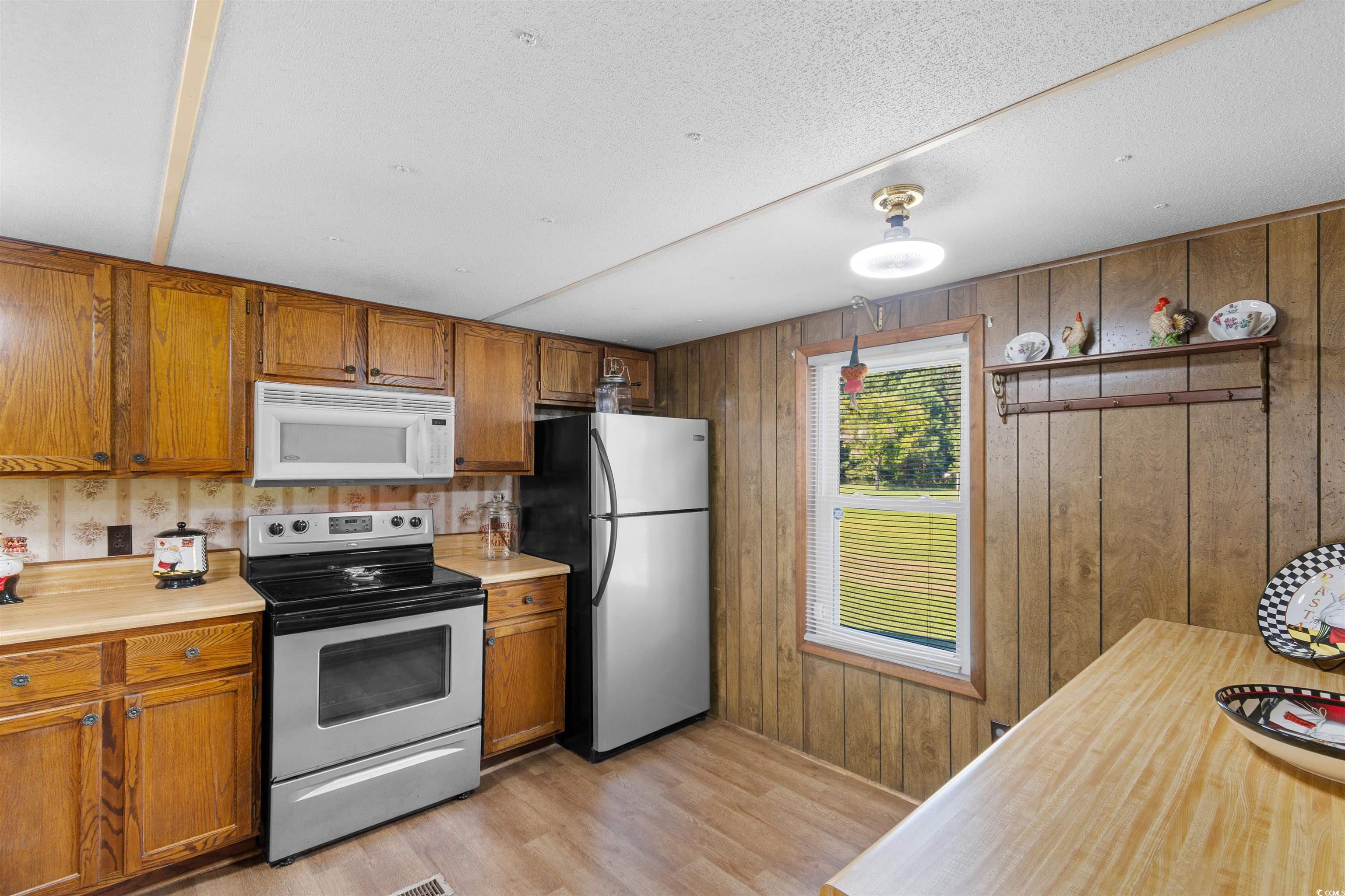 299 Williams Hill Road Hemingway, SC 29554 - Photo 13 of 40 Kitchen featuring light countertops, appliances with stainless steel finishes, brown cabinetry, light wood-style flooring, and wooden walls