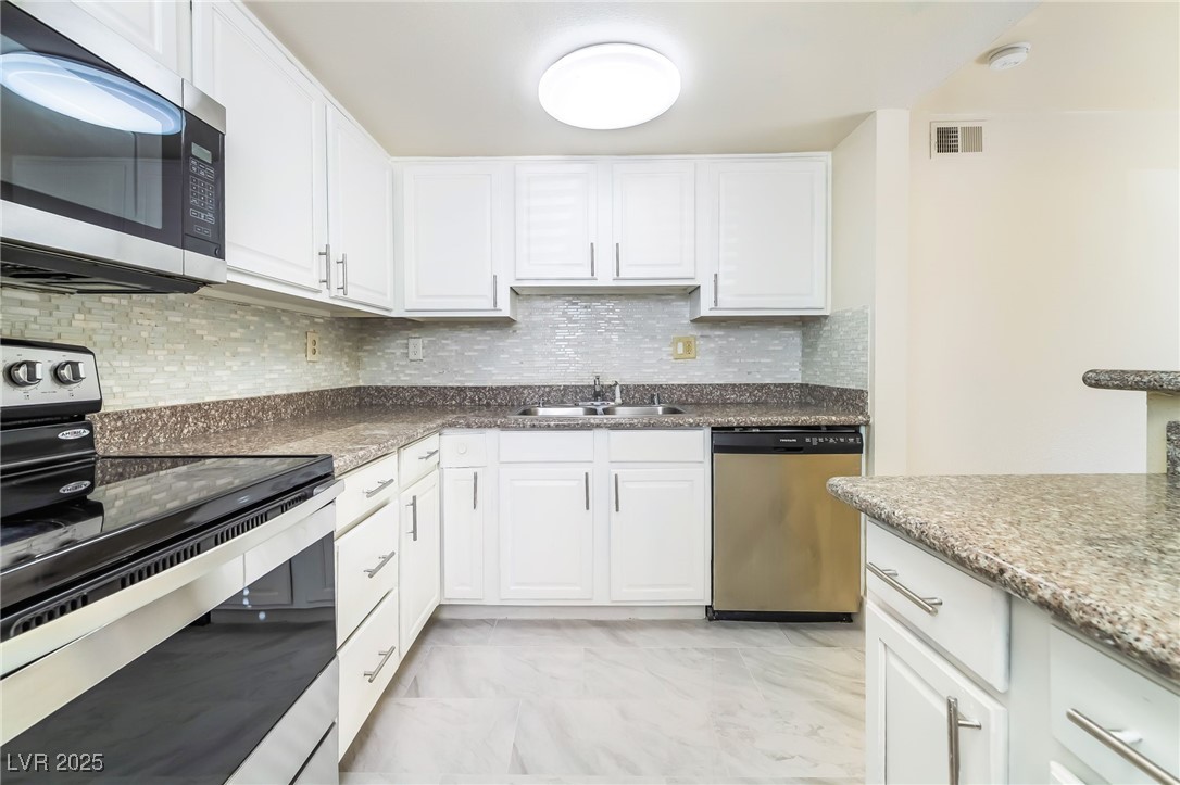 Kitchen featuring appliances with stainless steel finishes, white cabinets, decorative backsplash, light marble finish floors, and dark stone counters