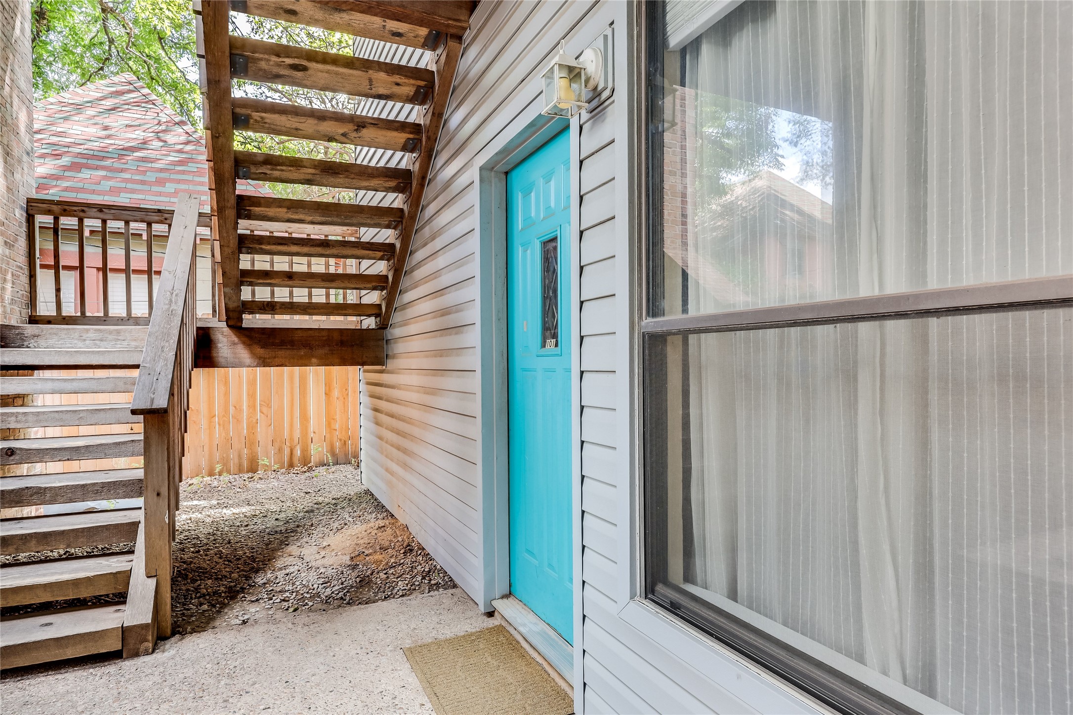 3011 Fruth Street, Unit 101 Austin, TX 78705 - Photo 2 of 14 A vibrant teal door invites entry, complemented by the weathered charm of the adjacent wooden staircase.