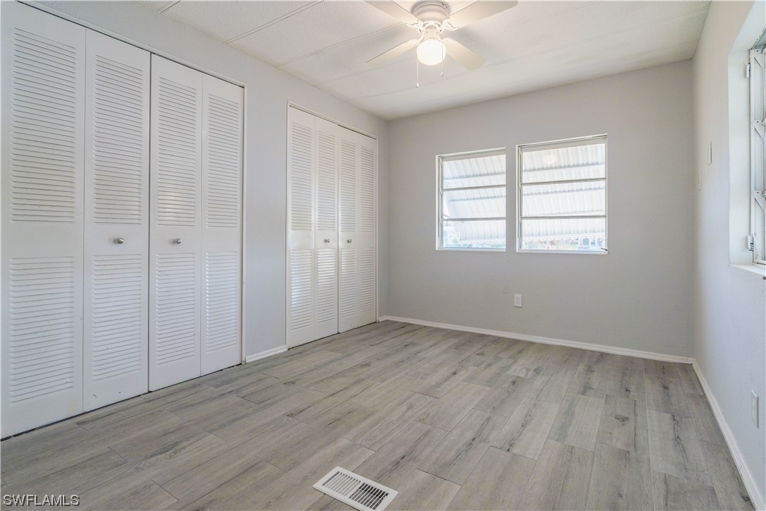 153 Cape Sable Drive Naples, FL 34104 - Photo 21 of 35 an empty room with wooden floor chandelier fan and windows