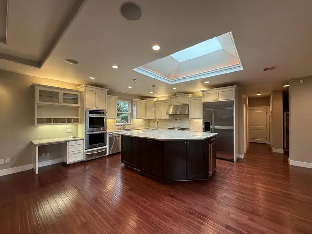 a view of kitchen with stainless steel appliances wooden floor and living room