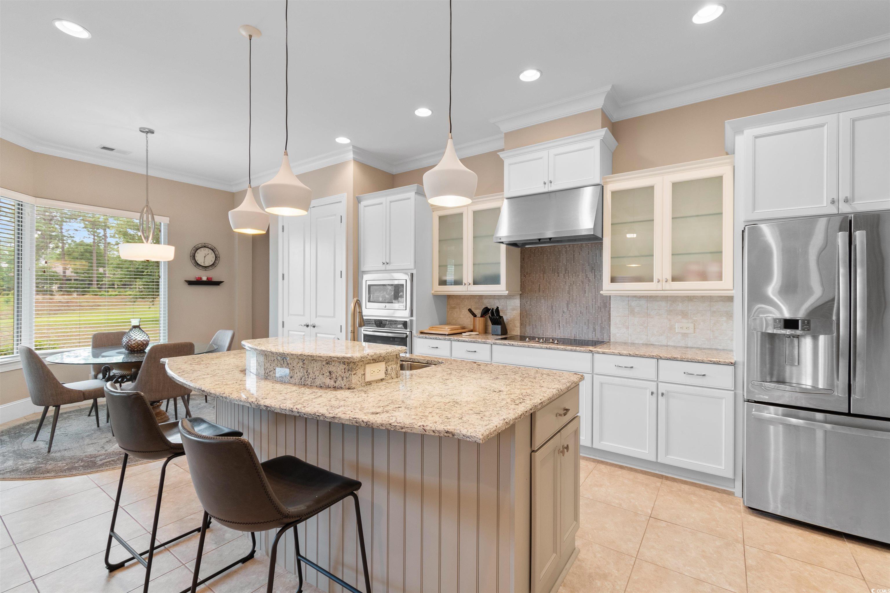 7253 Seville Drive Myrtle Beach, SC 29572 - Photo 10 of 39 Kitchen featuring appliances with stainless steel finishes, under cabinet range hood, light tile patterned floors, decorative backsplash, and a breakfast bar area