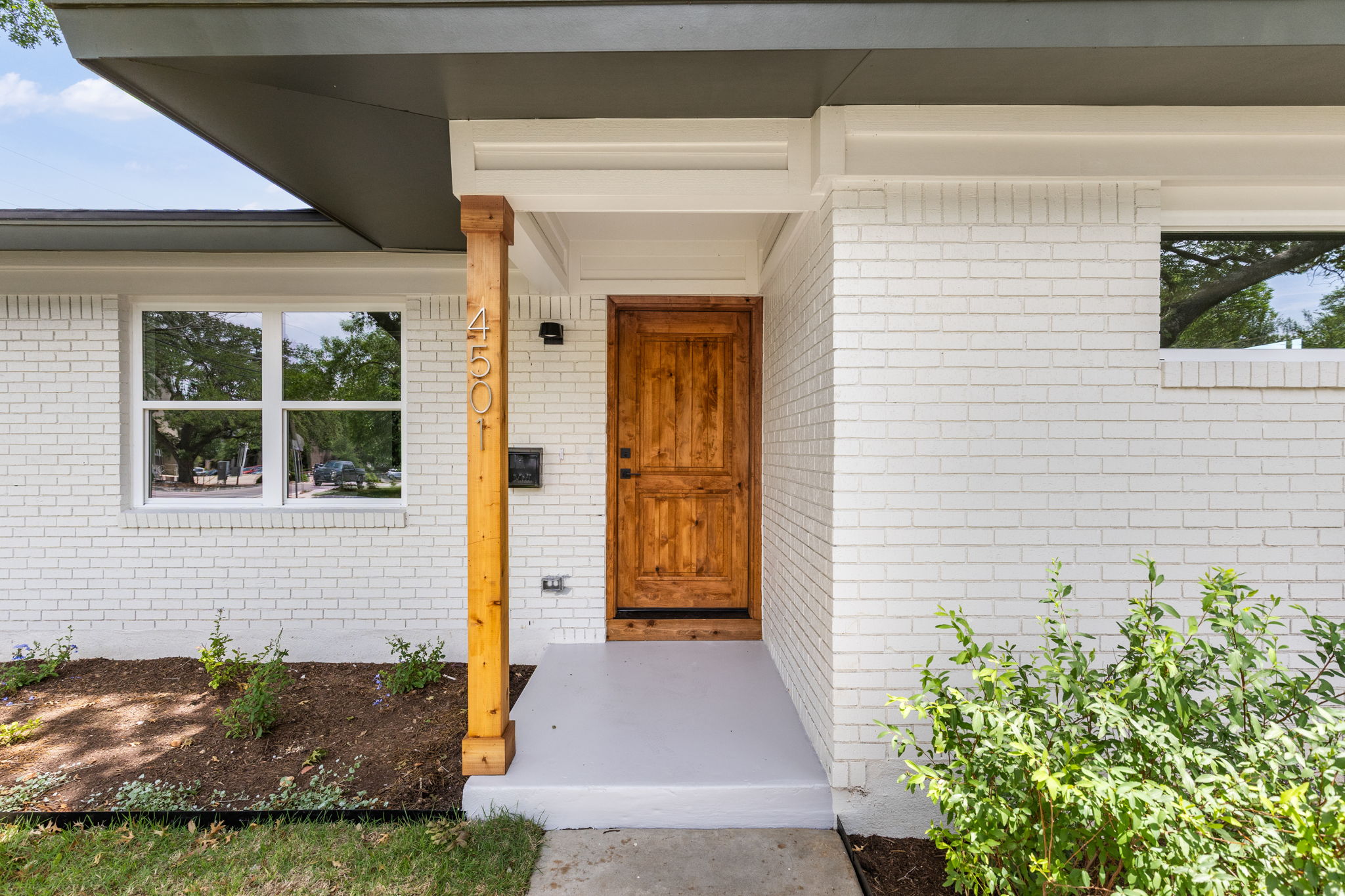 4501 Pack Saddle Pass Austin, TX 78745 - Photo 2 of 37 White brick exterior featuring a wood-panel entry door, wood support column with house numbers, and a concrete porch