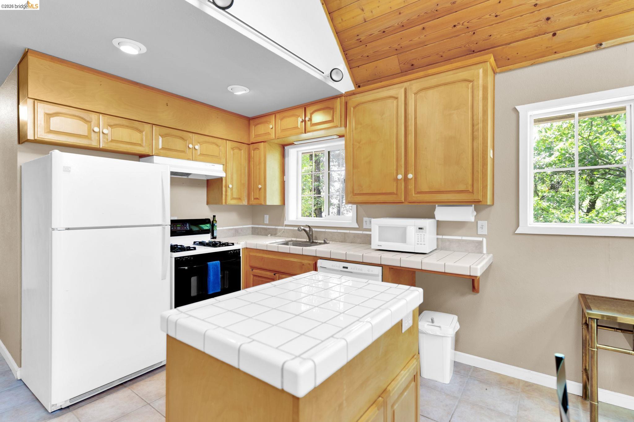 14799 Big Hill Road Sonora, CA 95370 - Photo 52 of 60 Kitchen with white appliances, tile counters, a center island, light wood finish cabinets, and light tile patterned floors
