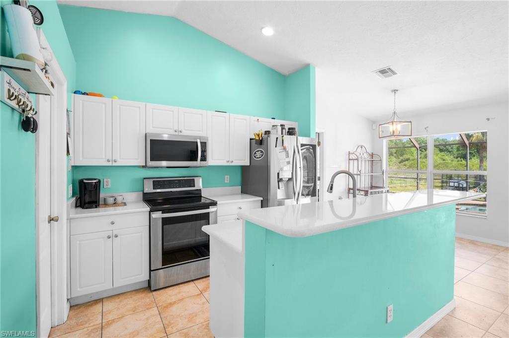 Kitchen featuring stainless steel appliances, light countertops, white cabinets, light tile patterned floors, and hanging light fixtures