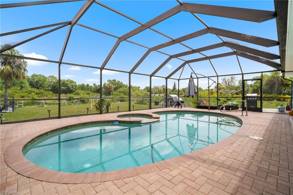 15601 Cemetery Road Fort Myers, FL 33905 - Photo 14 of 20 View of swimming pool with a pool with connected hot tub, a patio area, view of wooded area, a grill, and glass enclosure