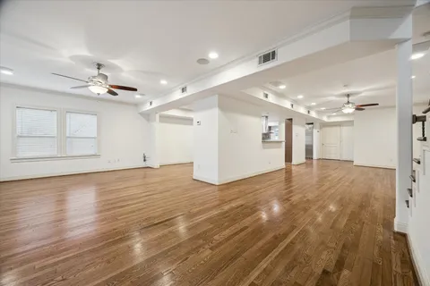 a view of an empty room with wooden floor and a ceiling fan
