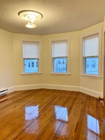 a view of an empty room with wooden floor and a fan