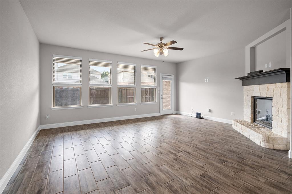 119 Happy Lane Red Oak, TX 75154 - Photo 7 of 37 Spacious living area featuring wood-finish flooring, a stone-clad fireplace with a dark mantel, and multiple windows with blinds