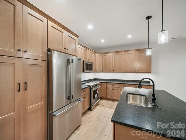 a kitchen with stainless steel appliances granite countertop a refrigerator a sink a stove and a sink with wooden floor