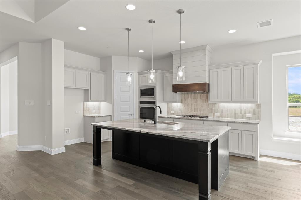 708 Splendor Drive McKinney, TX 75072 - Photo 11 of 29 a kitchen with kitchen island granite countertop a sink a center island stainless steel appliances and a window