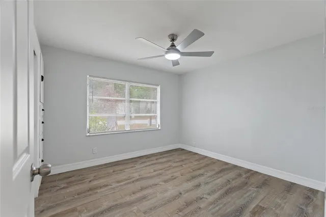an empty room with wooden floor ceiling fan and windows