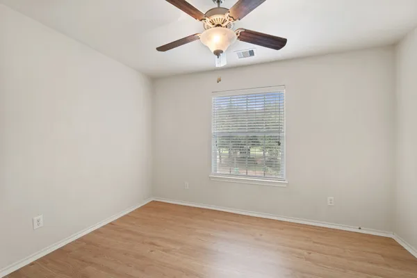 an empty room with wooden floor chandelier fan and windows