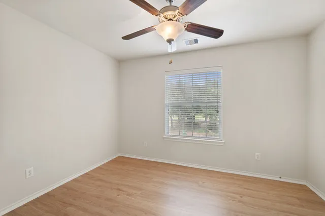 an empty room with wooden floor chandelier fan and windows