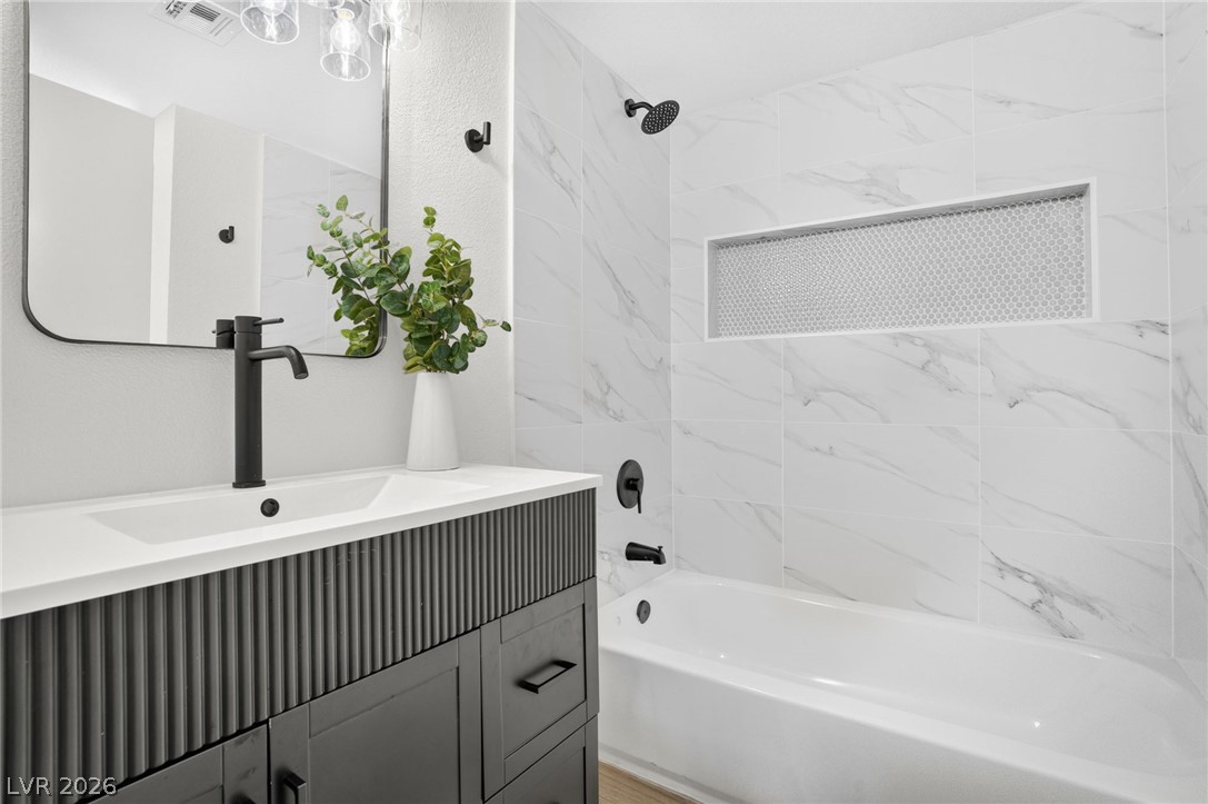2681 Rungsted Street Las Vegas, NV 89142 - Photo 23 of 33 A well-appointed bathroom features a modern vanity with a sleek black faucet and a bathtub encased in elegant white marble-patterned tile.