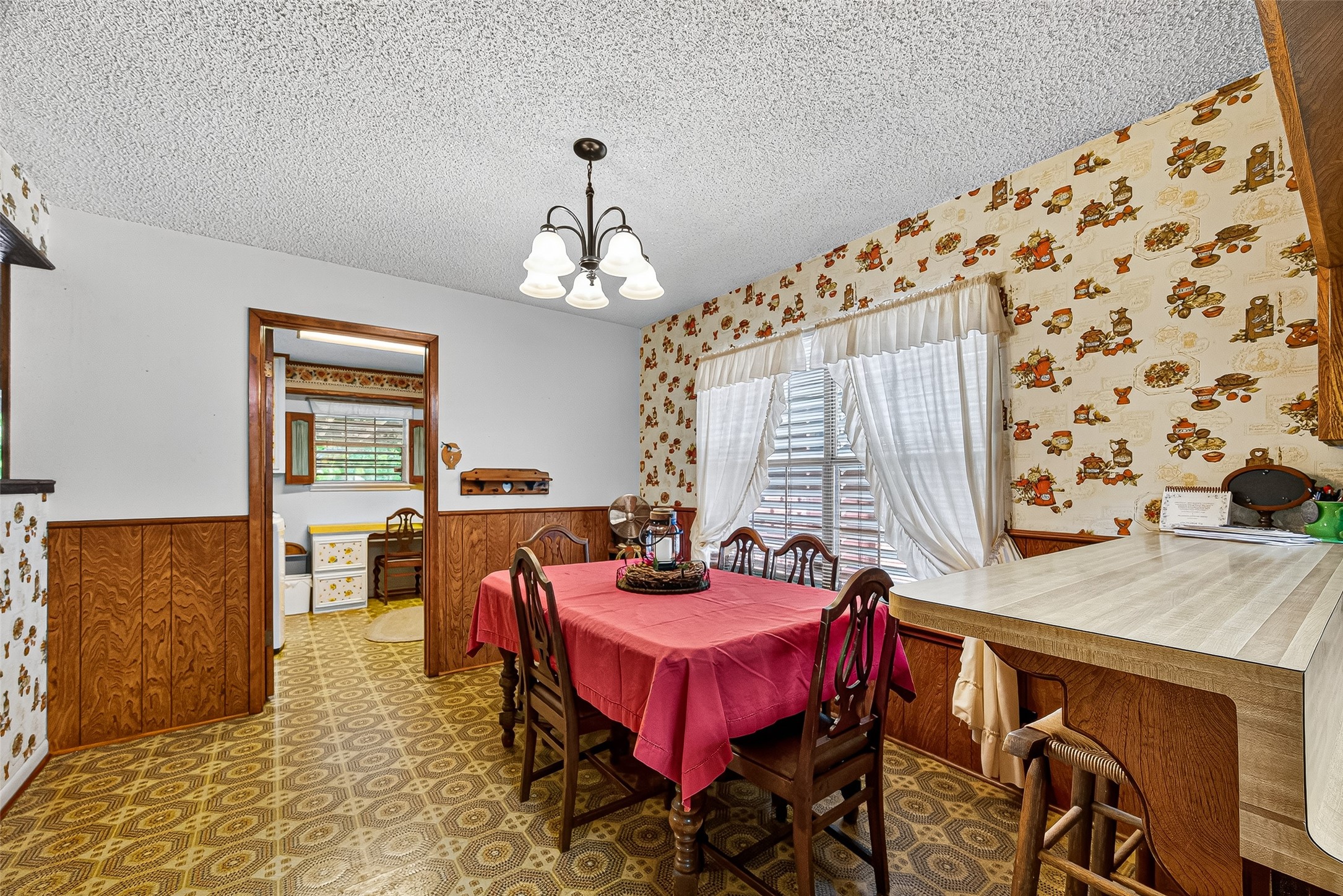 12021 7th 1/2 Street Santa Fe, TX 77510 - Photo 23 of 49 This cozy dining area features vintage wallpaper and wood paneling, with a bright window and overhead lighting. The space connects to a kitchen through a doorway, and includes a practical breakfast bar for additional seating.