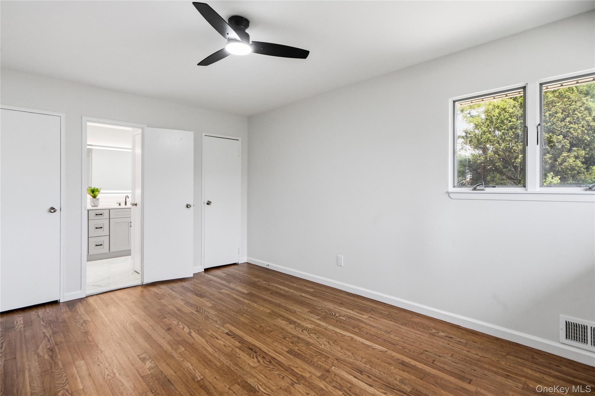 183 North Marginal Road Jericho, NY 11753 - Photo 16 of 28 Primary bedroom featuring wood-finish flooring, a modern black ceiling fan with integrated lighting, and two windows providing natural light with access to bathroom
