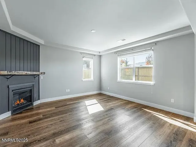 a view of an empty room with wooden floor fireplace and a window