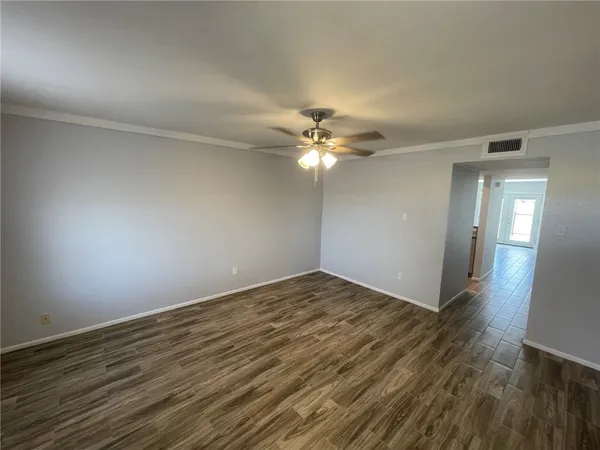 a view of an empty room with wooden floor and chandelier fan