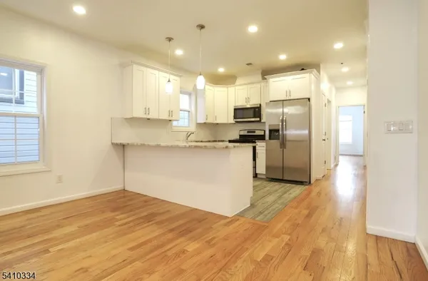 a kitchen with stainless steel appliances granite countertop a refrigerator a sink dishwasher a stove and white cabinets with wooden floor