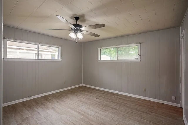an empty room with wooden floor fan and windows