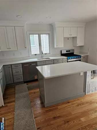 a living room with stainless steel appliances granite countertop a dishwasher a stove a sink and white cabinets with wooden floor