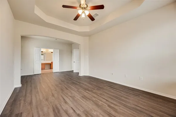 an empty room with wooden floor ceiling fan and windows