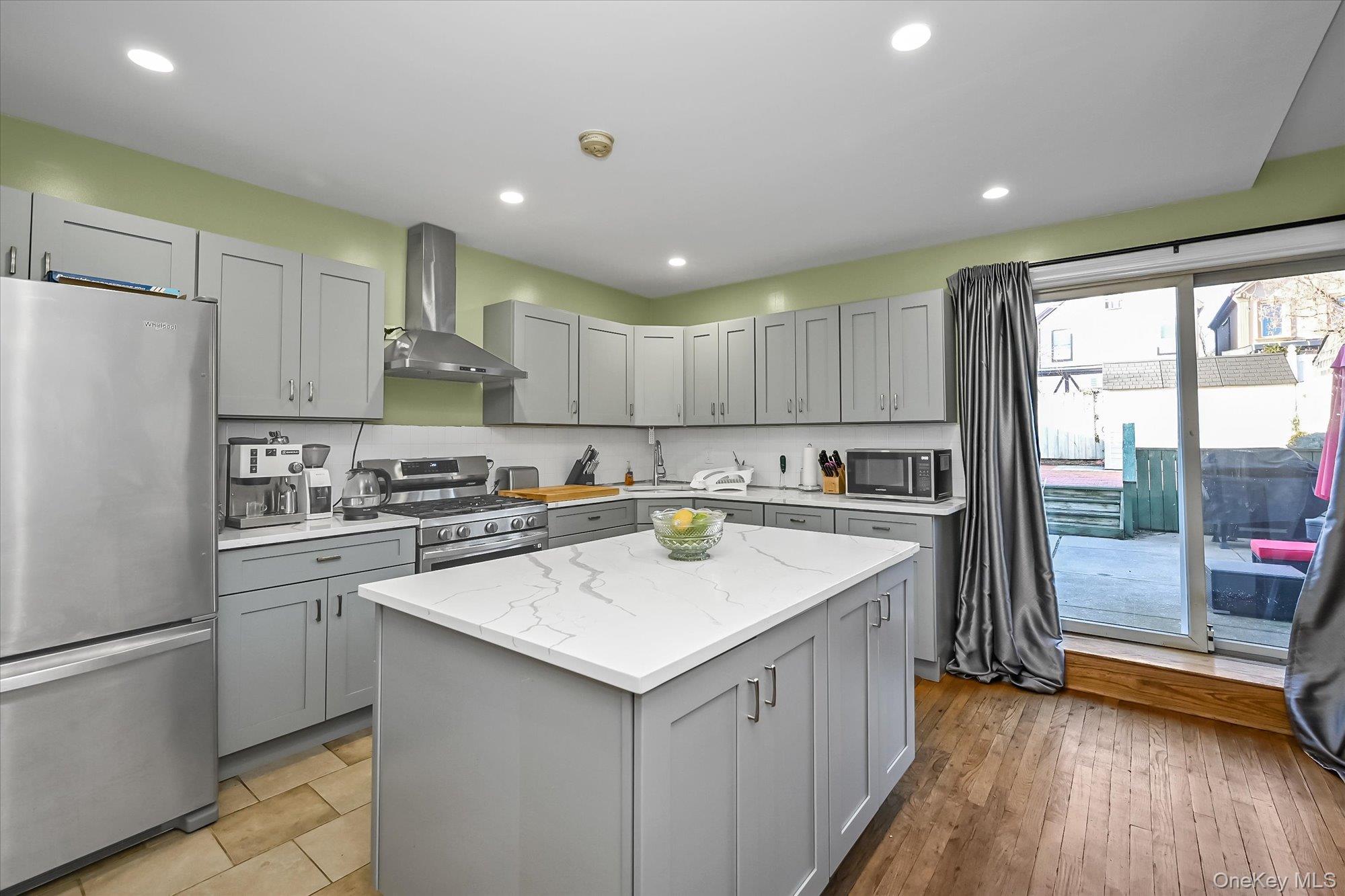 69-25 59th Road Queens, NY 11378 - Photo 7 of 24 Kitchen featuring stainless steel appliances, wall chimney exhaust hood, a kitchen island, light stone countertops, and gray cabinets