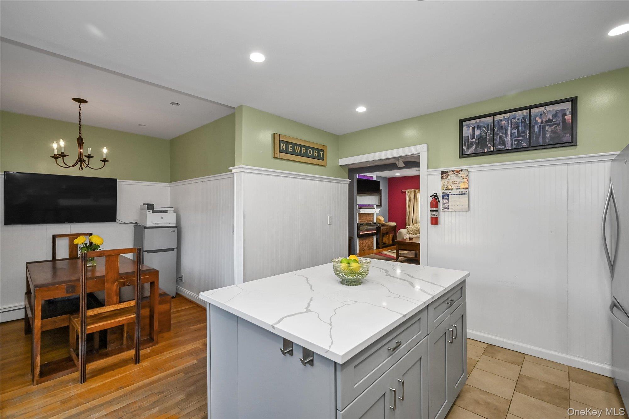 69-25 59th Road Queens, NY 11378 - Photo 8 of 24 Kitchen featuring a center island, gray cabinetry, a chandelier, decorative light fixtures, and light stone counters