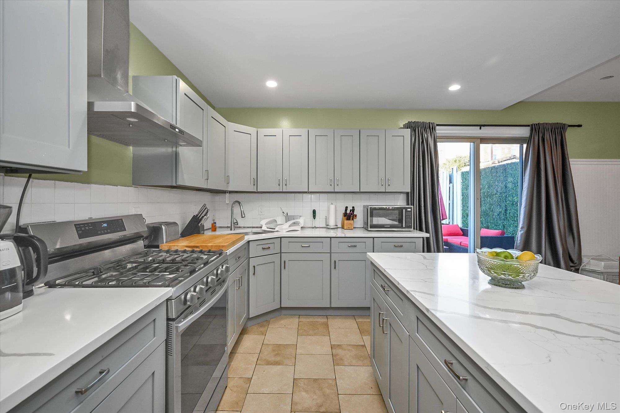 69-25 59th Road Queens, NY 11378 - Photo 9 of 24 Kitchen with stainless steel appliances, wall chimney exhaust hood, gray cabinetry, tasteful backsplash, and light stone countertops