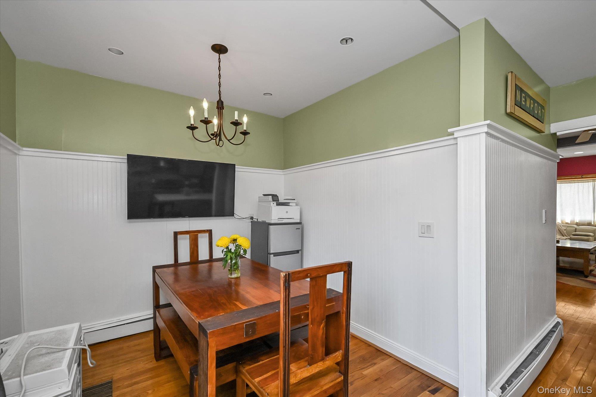 69-25 59th Road Queens, NY 11378 - Photo 10 of 24 Dining area with a baseboard heating unit, wood-type flooring, a chandelier, wainscoting, and baseboard heating