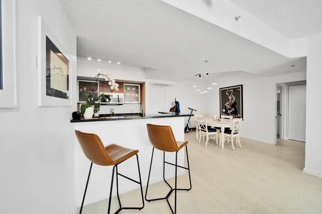 a kitchen with stainless steel appliances kitchen island granite countertop a dining table chairs and a refrigerator