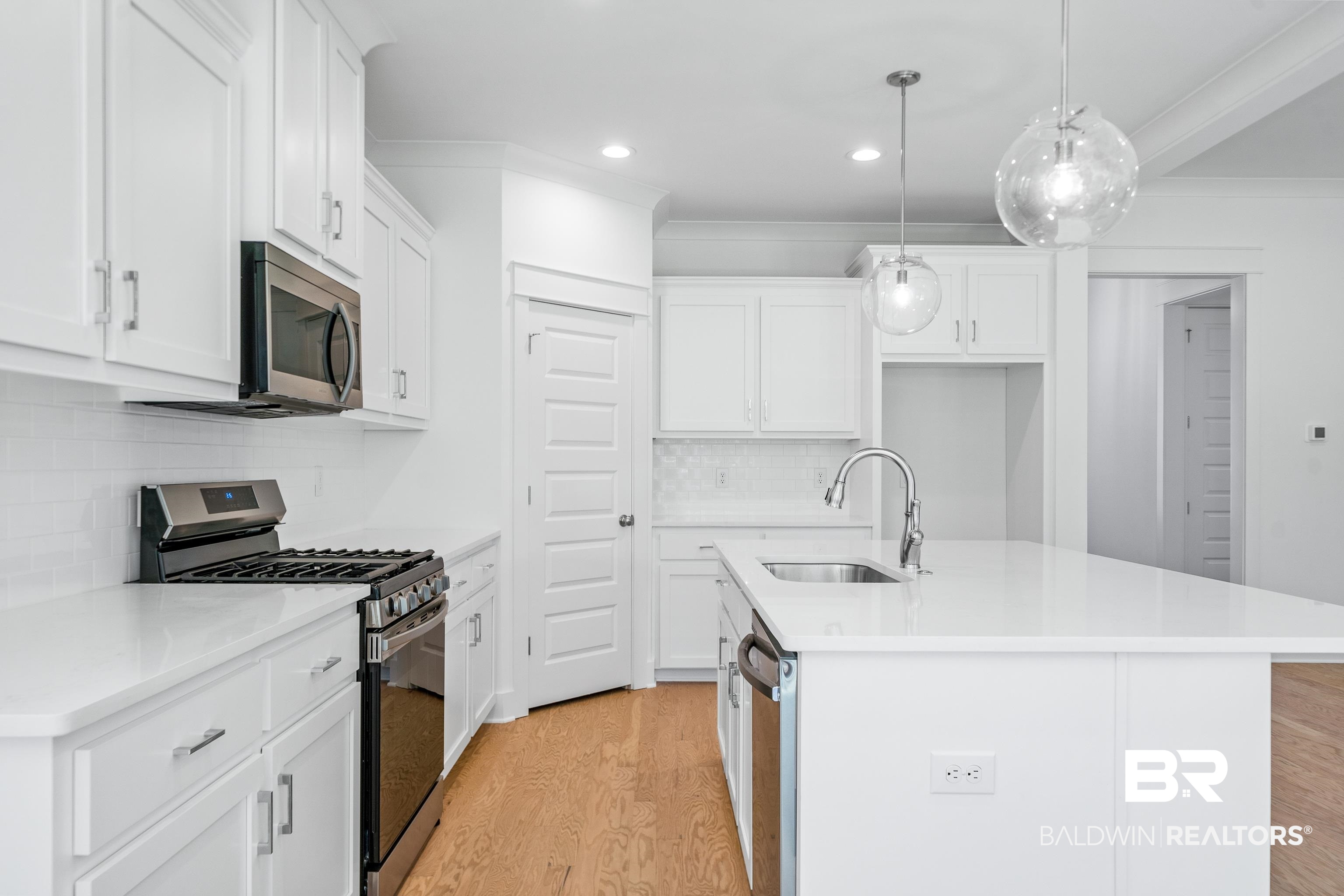 25927 Capra Court Daphne, AL 36526 - Photo 12 of 37 Kitchen featuring decorative light fixtures, a center island with sink, white cabinetry, stainless steel appliances, and light hardwood / wood-style floors