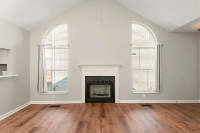 an empty room with wooden floor fireplace and windows