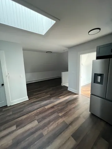 a view of empty room with wooden floor and kitchen