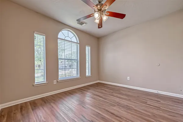 an empty room with wooden floor chandelier fan and windows