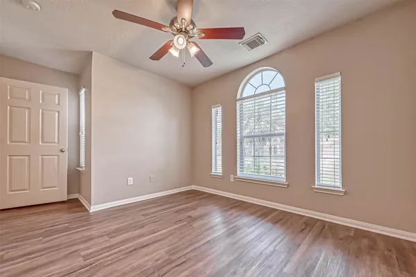 an empty room with wooden floor chandelier fan and windows