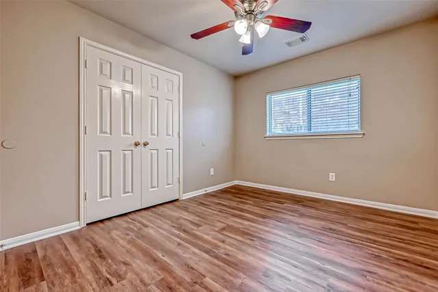an empty room with wooden floor chandelier fan and windows