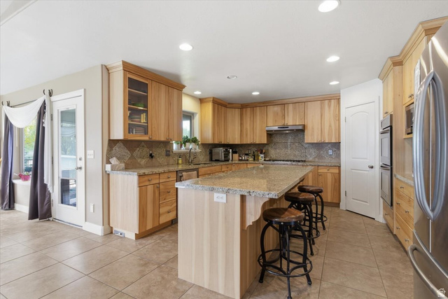 6237 West 4600th Street South Hooper, UT 84315 - Photo 12 of 48 Kitchen featuring light stone countertops, a kitchen breakfast bar, stainless steel appliances, a center island, and glass insert cabinets