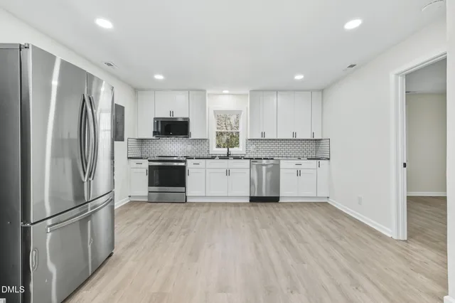 a kitchen with stainless steel appliances granite countertop a refrigerator a stove a sink and white cabinets with wooden floor