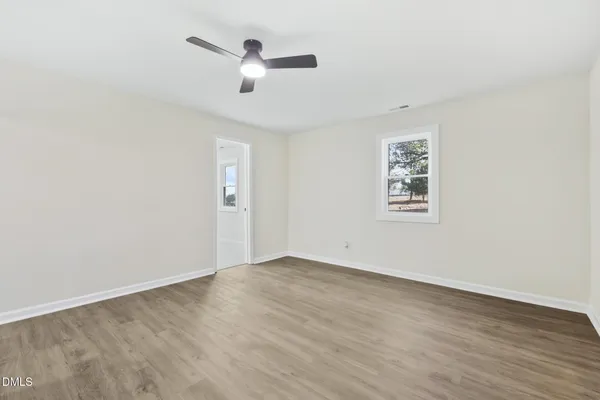 an empty room with wooden floor chandelier fan and windows