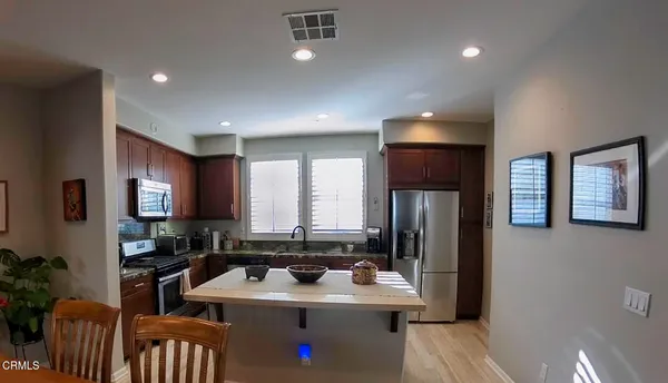a kitchen with stainless steel appliances granite countertop a refrigerator a sink a stove a dining table and chairs