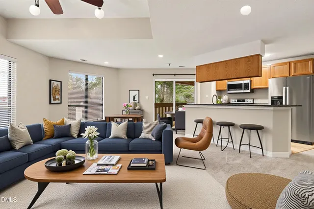 a living room with furniture a rug kitchen view and a large window