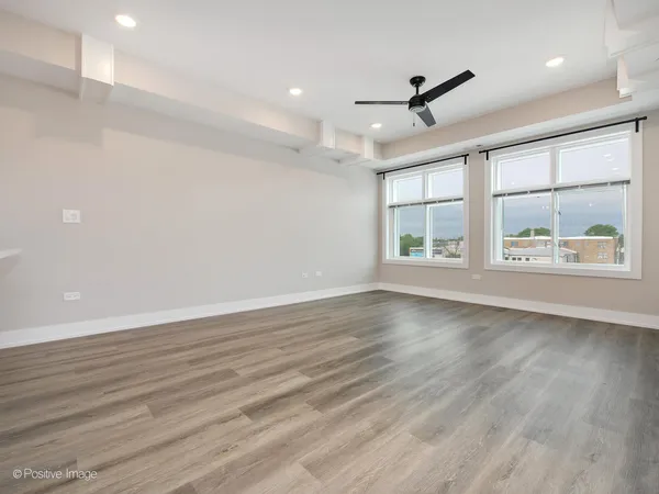 an empty room with wooden floor ceiling fan and windows