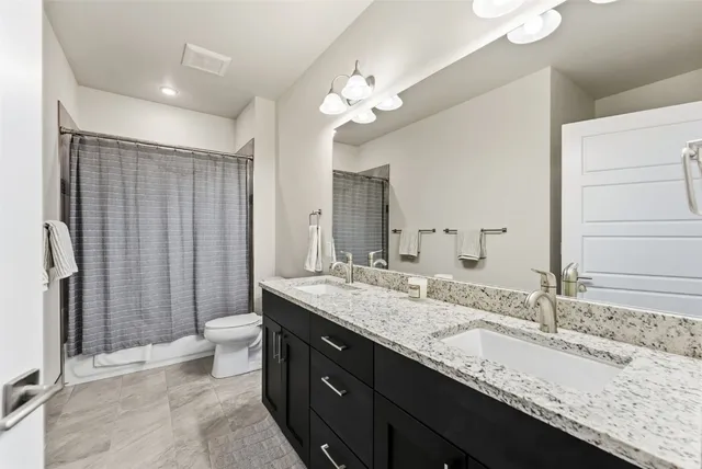 a bathroom with a granite countertop sink a toilet a large mirror and shower