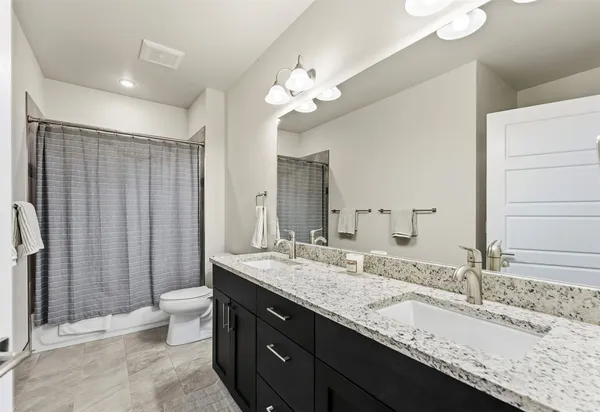 a bathroom with a granite countertop double vanity sink mirror and toilet
