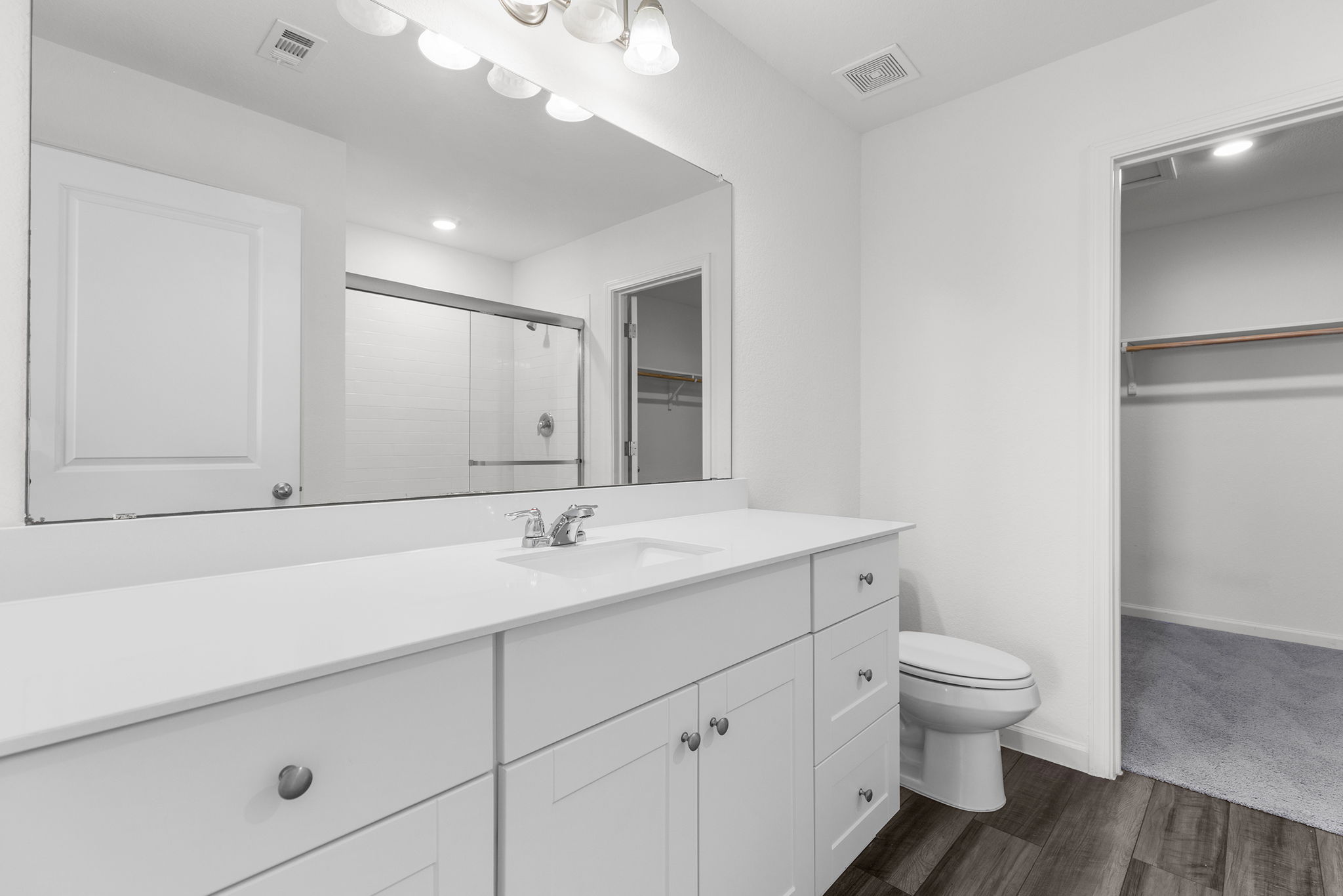 409 Line Of Fire Way Jarrell, TX 76537 - Photo 20 of 30 Contemporary bathroom featuring a large vanity with white cabinetry, single integrated sink, spacious mirror, chrome fixtures, wood-finish flooring, and neutral wall paint.