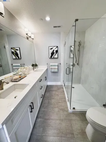 a spacious bathroom with a double vanity sink a toilet a mirror and shower